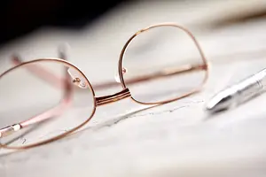 A close-up view of a pair of glasses with a silver pen placed on top of a piece of paper, possibly in an office setting.
