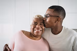 An adult man is kissing a woman's forehead while she is smiling in a room with white walls.