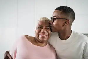 An adult man is kissing a woman's forehead while she is smiling in a room with white walls.