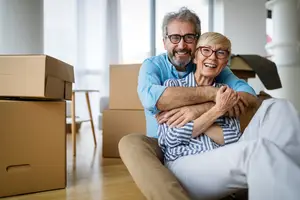 Senior couple moving into their new home, sitting on the floor and smiling with boxes around them.