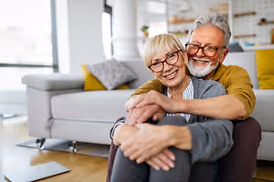 A couple sitting on a couch in their home, smiling and embracing each other