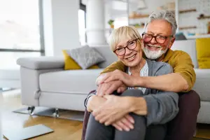 A couple sitting on a couch in their home, smiling and embracing each other