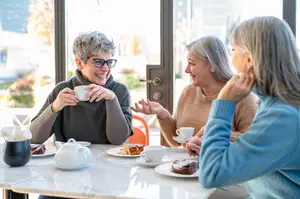 Three women sitting around a table having a conversation while holding a cup and a plate of desserts