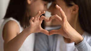 A mother and daughter making a heart shape with their hands.