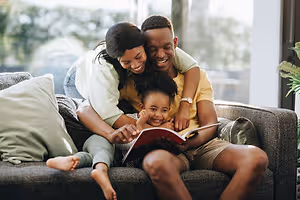 A family sitting on a couch, with the parents reading a book to their child