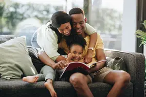 A family sitting on a couch, with the parents reading a book to their child
