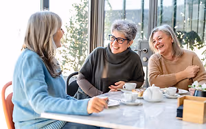 Three women sitting at a table, laughing and enjoying their coffee and tea