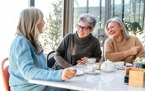 Three women sitting at a table, laughing and enjoying their coffee and tea
