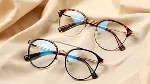 A pair of glasses with blue lenses and black frames is placed on a cream fabric cloth. The lenses reflect light and have a blue hue. The glasses are probably displayed in a store or a shop.