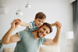 A man with a smiling child sitting on his shoulder in a room