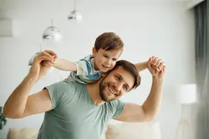 A man with a smiling child sitting on his shoulder in a room