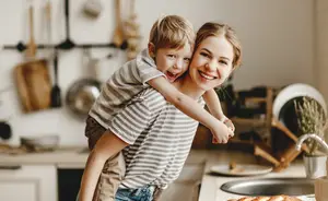 A woman carrying her son on her shoulder in a kitchen with a smiling face