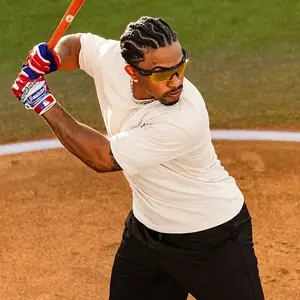 A man wearing a white t-shirt, black pants, and sunglasses is hitting a baseball with a baseball bat on a baseball field