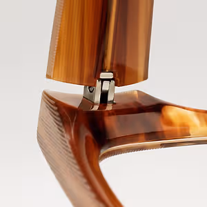A close-up view of the back of a chair with a curved, wooden seat and a metal hinge, the chair's frame is made of wood with a smooth finish, possibly made of horn, and the metal hinge is attached to the back of the chair, the chair's seat has a curved design with a smooth finish, possibly made of horn, the chair's frame is made of wood with a smooth finish, possibly made of horn, and the metal hinge is attached to the back of the chair.
