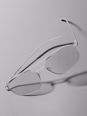 A close up of a pair of white frame glasses with clear lenses lying flat on a gray background