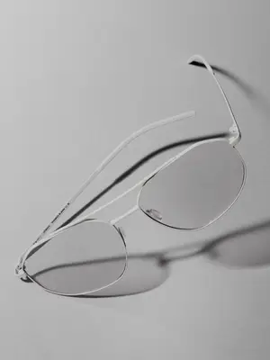 A close up of a pair of white frame glasses with clear lenses lying flat on a gray background