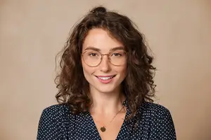 Portrait of a young woman with curly hair and glasses smiling for the camera