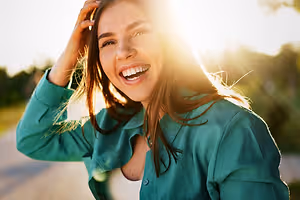 A woman in a green shirt smiles and laughs outside in the sunlight