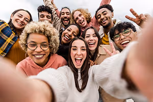 A group of people are smiling and posing for a photo, some are holding hands and one is making a peace sign