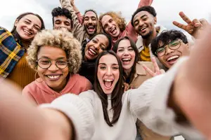 A group of people are smiling and posing for a photo, some are holding hands and one is making a peace sign