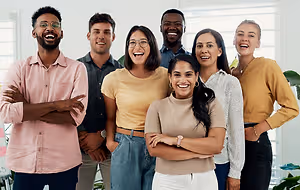 A group of people standing together and smiling in a room with white walls and a plant in the corner