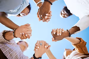 a group of people holding hands in a circle under a blue sky