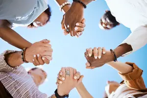 a group of people holding hands in a circle under a blue sky