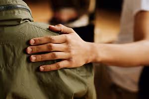 A person is holding the shoulder of another person who is wearing a green jacket