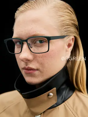 A woman with freckles wearing a black leather collar with a silver button and glasses.