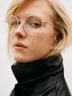 A woman with freckles is wearing a black jacket and glasses with a logo on the lens.