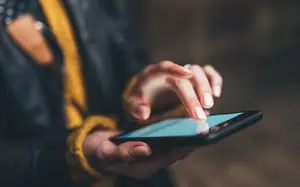 A person is holding a smartphone with a finger on the screen.