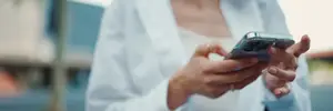 A woman in a white shirt is holding a cell phone and looking at it.