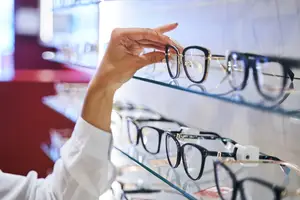 A person is holding a pair of eyeglasses with a blurry background