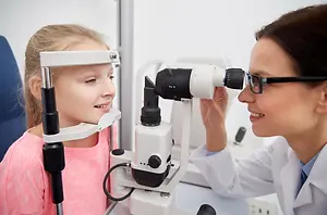 A woman optometrist is checking the eyes of a little girl using an ophthalmoscope.