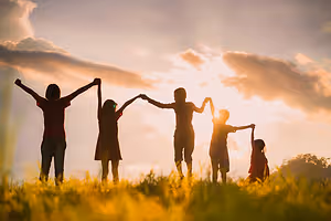 Five people holding hands in a field at sunset