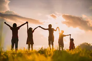 Five people holding hands in a field at sunset