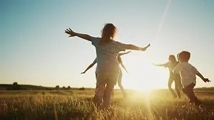 A group of children are playing in the grassy field with the sun shining brightly on them
