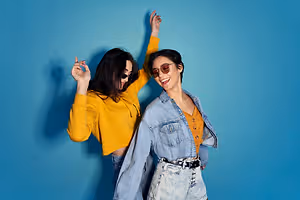 Two women posing for a picture with one holding up her arm while the other stands beside her with her arms up