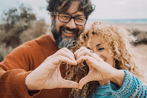 A couple making a heart shape with their hands on a beach