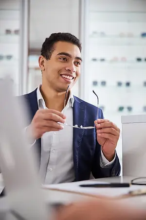 a man sitting in a chair and smiling while holding a pair of glasses