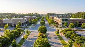Aerial view of a landscaped commercial district with tree-lined streets, modern buildings, and wooded hills beyond