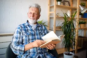 A senior man sits in his chair and reads a book in his home