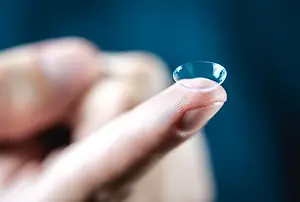A close up of a fingertip with a small lens, likely a contact lens, resting on it.