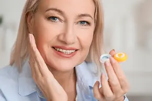 A woman holding a contact lens in her hand and smiling
