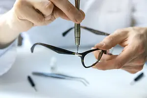 A person is repairing a pair of glasses using a screwdriver.