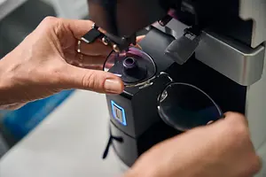 A person holding a pair of glasses is using a machine to adjust the lenses.