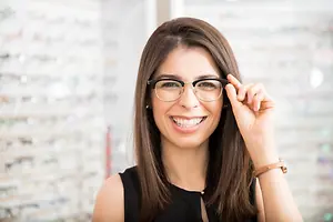 A woman with glasses is smiling and holding her glasses in front of her face.