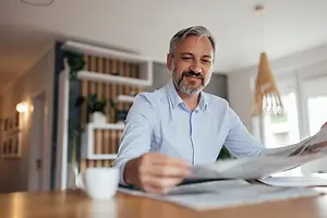 A man sitting in a room, reading a newspaper and smiling