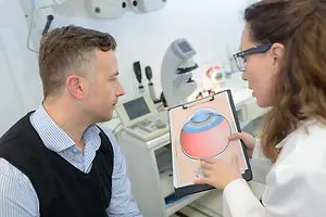 A man and a woman in a clinic, the woman shows the man a diagram of an eye on a clipboard