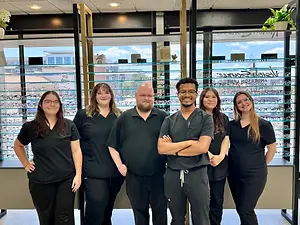 Six optometry clinic staff members posing together in front of an eyeglass display